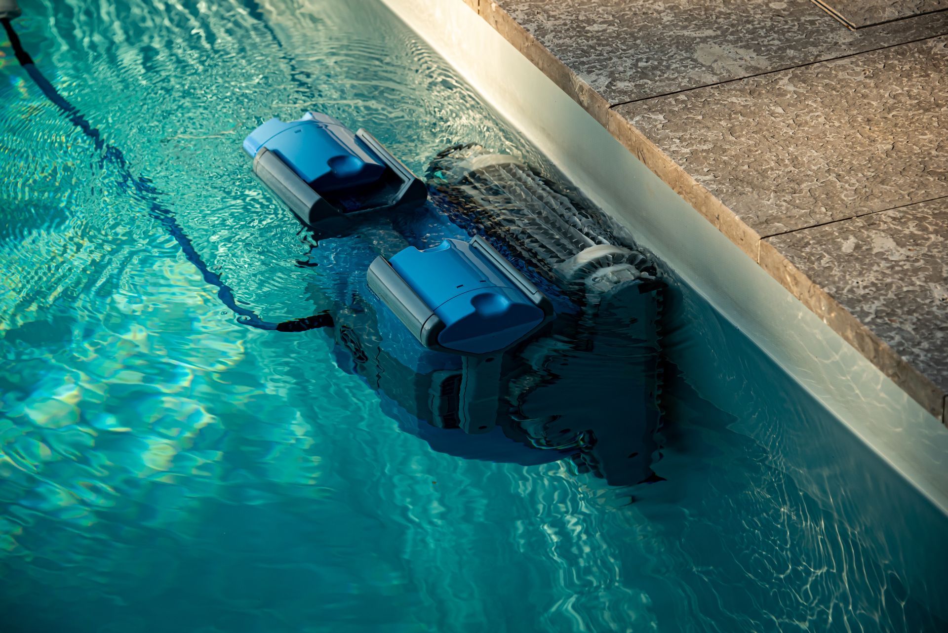 A blue robotic pool cleaner scrubs the waterline of a swimming pool.