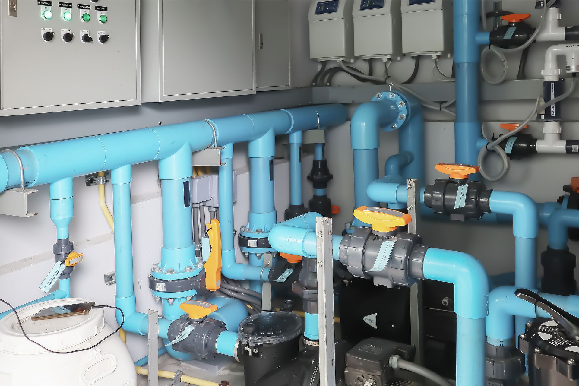 A complex network of blue industrial pipes, valves, and electrical control panels in a water treatment system.