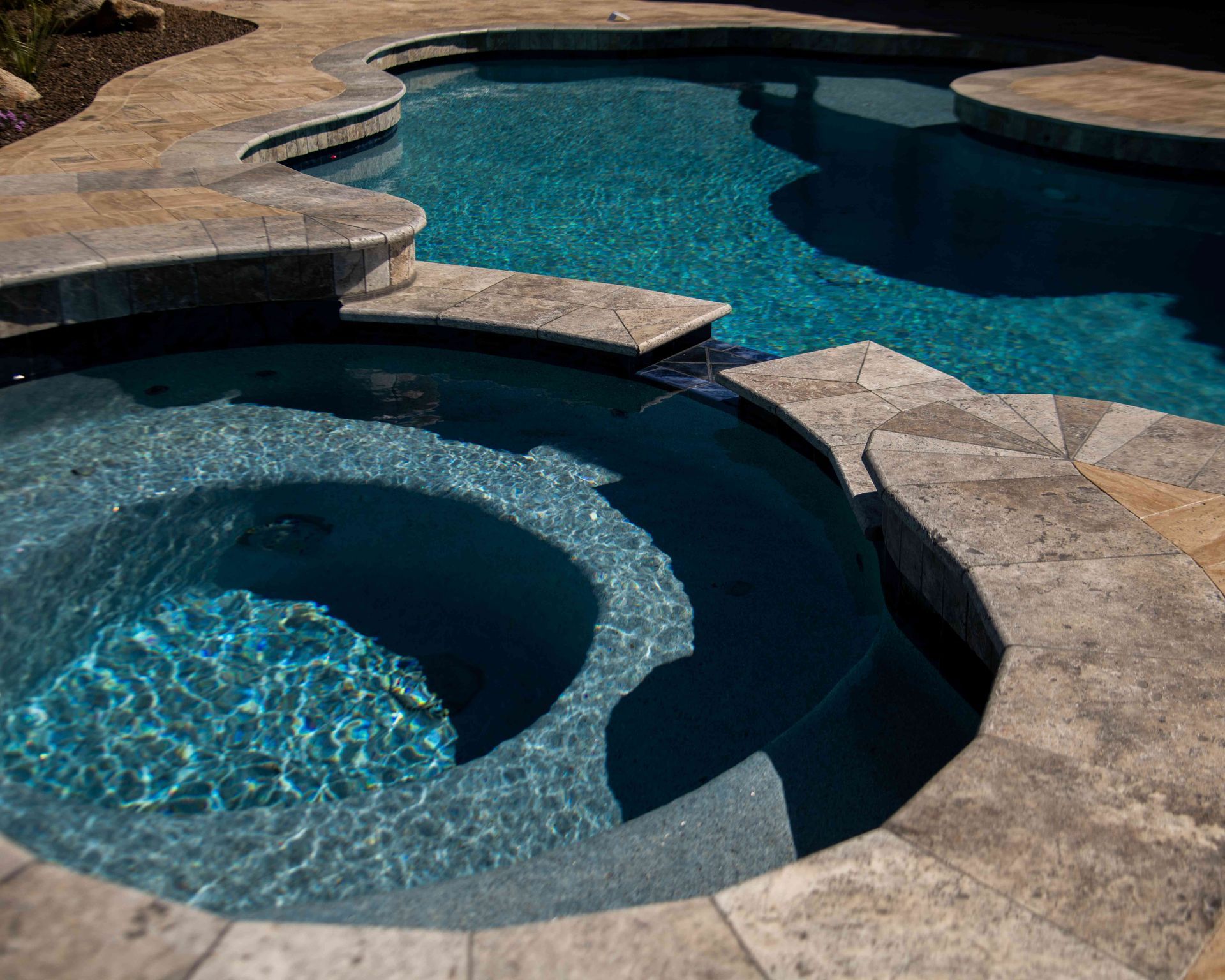 Backyard pool with a circular hot tub and curved stone decking in sunlight