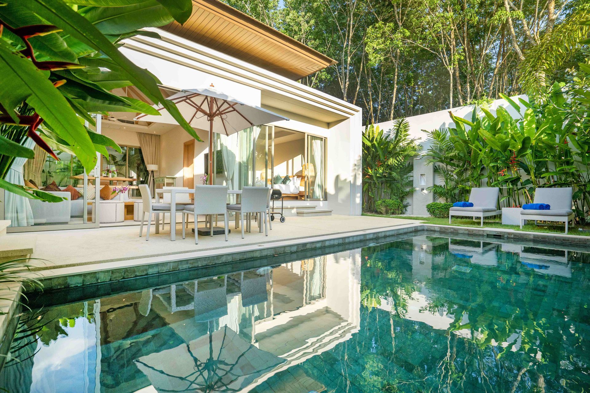 Modern house patio with a dining area beside a clear blue swimming pool and lush greenery