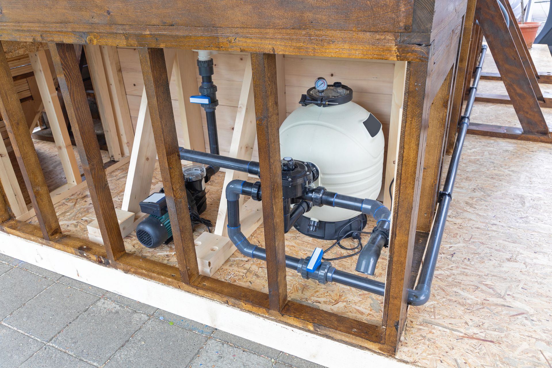 A swimming pool pump and white sand filter system installed inside a wooden framework structure.