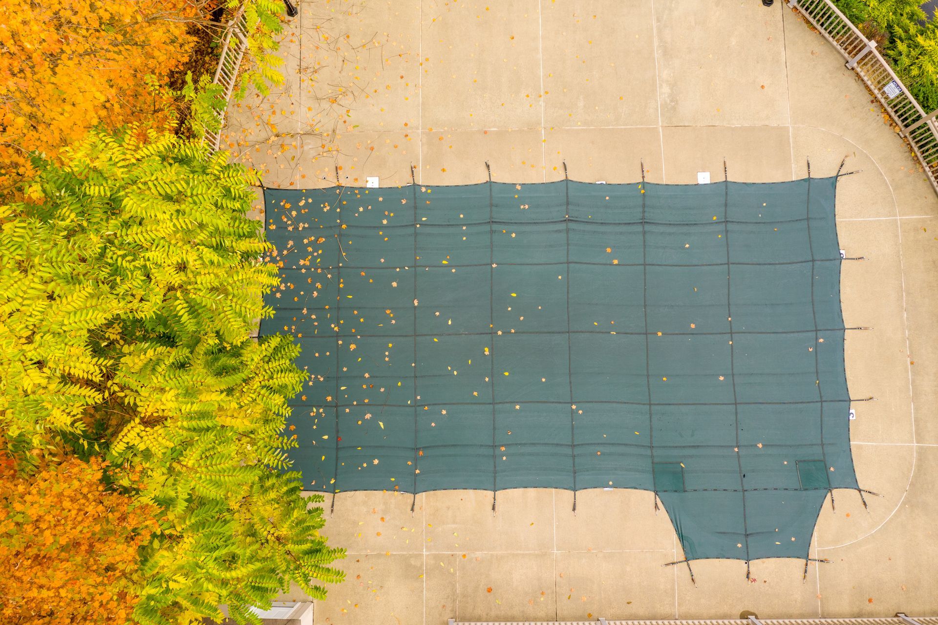 An aerial view of a rectangular, dark green swimming pool cover on a concrete deck.
