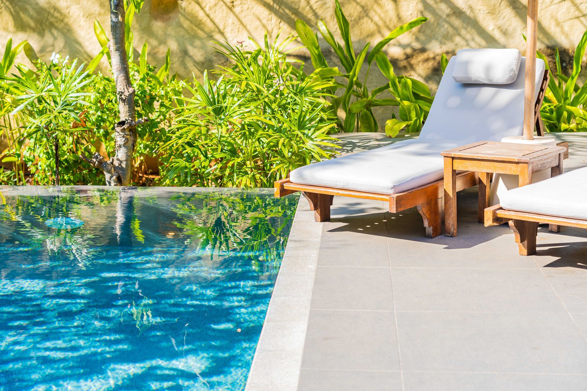 Poolside lounge chairs beside a turquoise pool in a sunny tropical setting