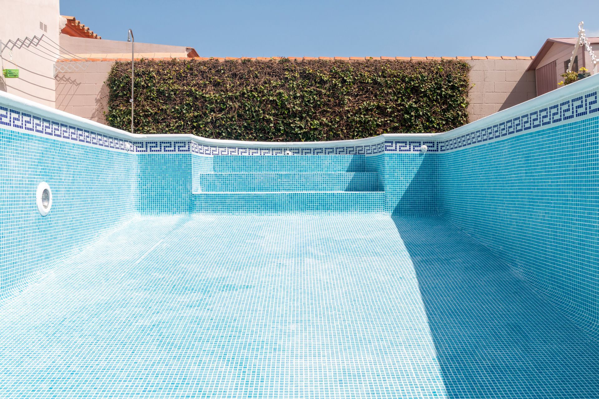 An empty, tiled rectangular swimming pool with blue and white mosaic patterns and steps at the far end.