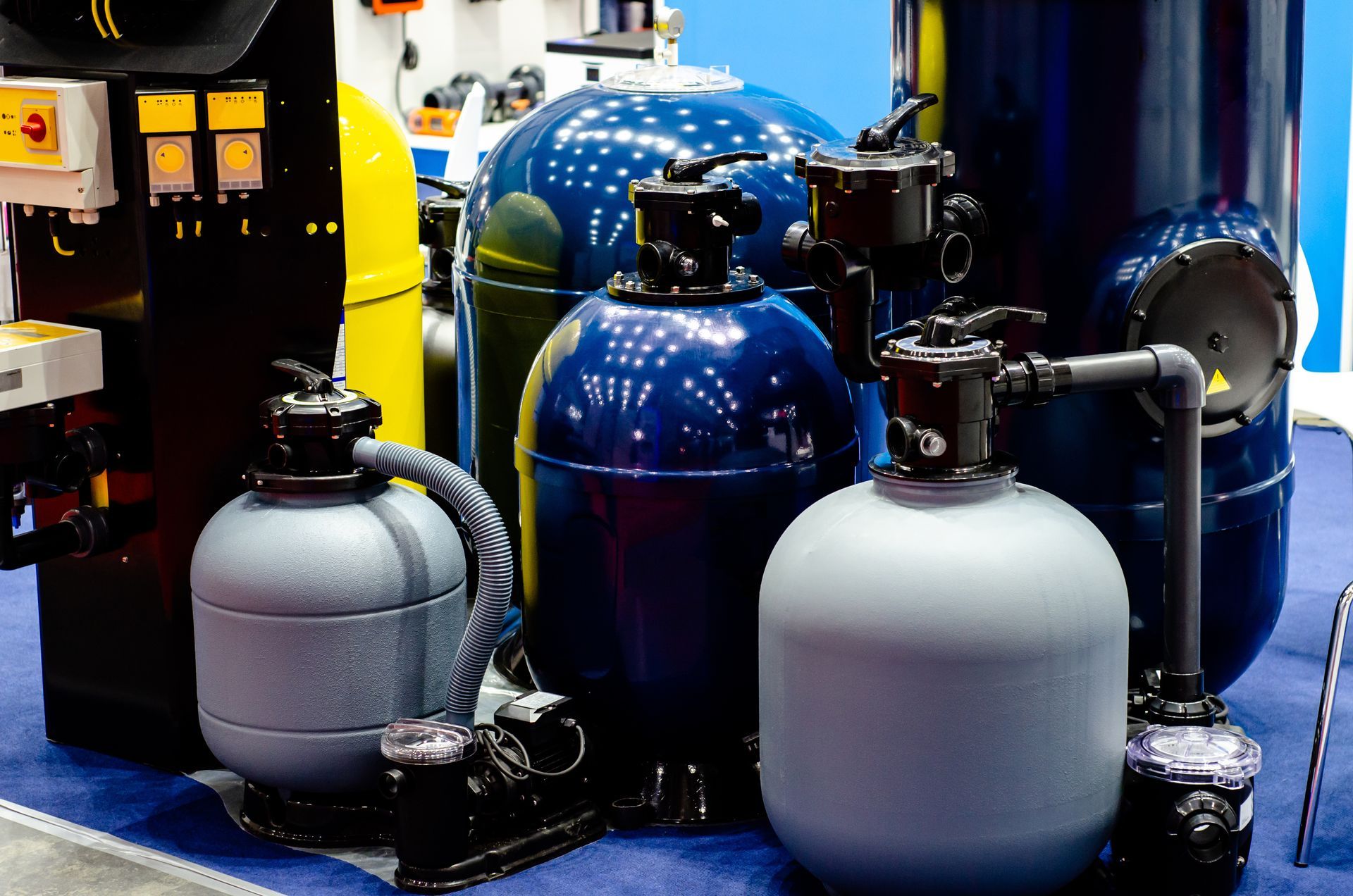 Several industrial and residential water filtration tanks in shades of dark blue and grey, arranged on a blue surface.