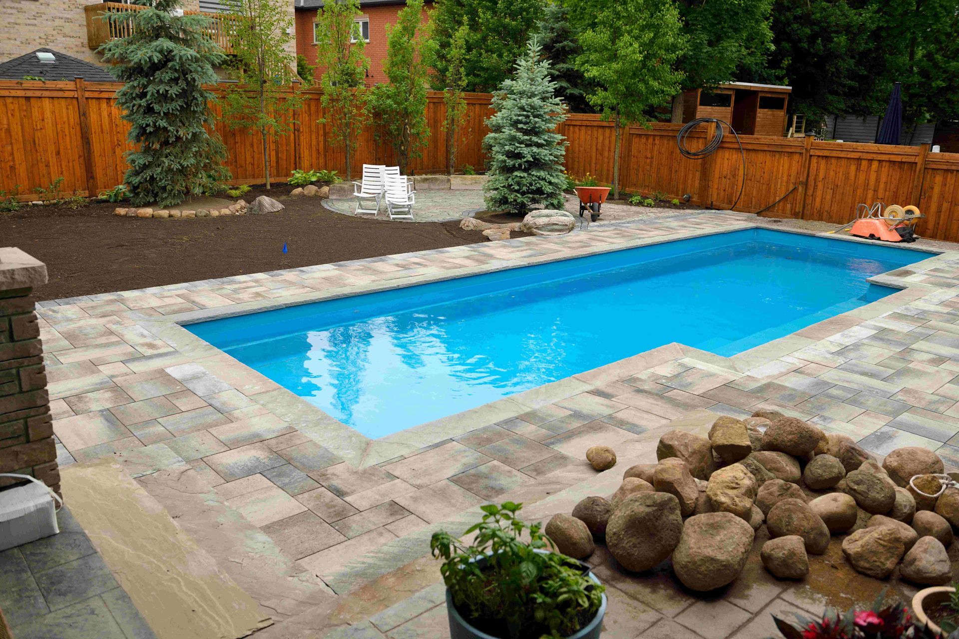Backyard with rectangular blue swimming pool, stone patio, wooden fence, and landscaping stones
