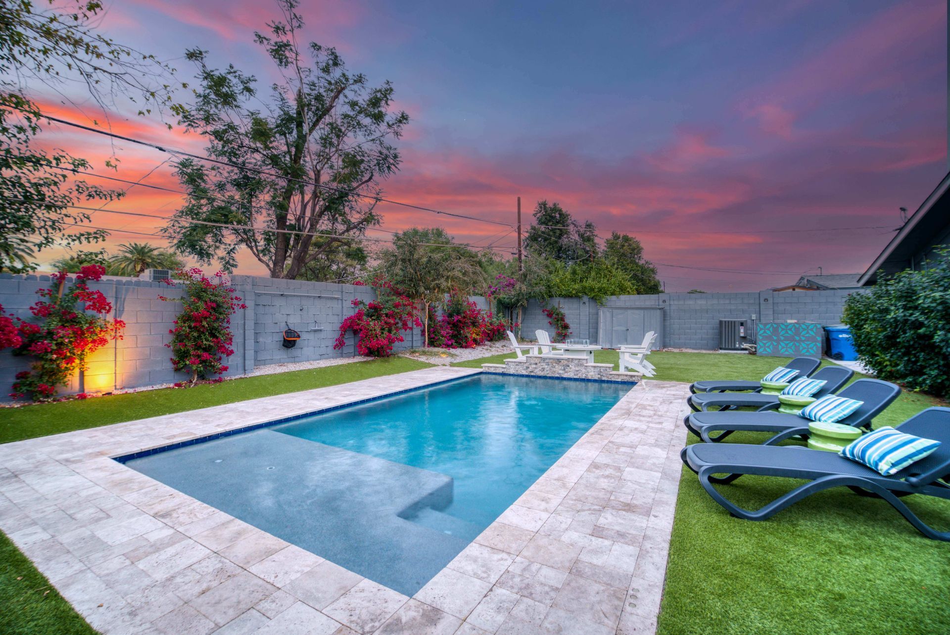 Backyard pool at sunset with lounge chairs, green lawn, and a pink-purple sky