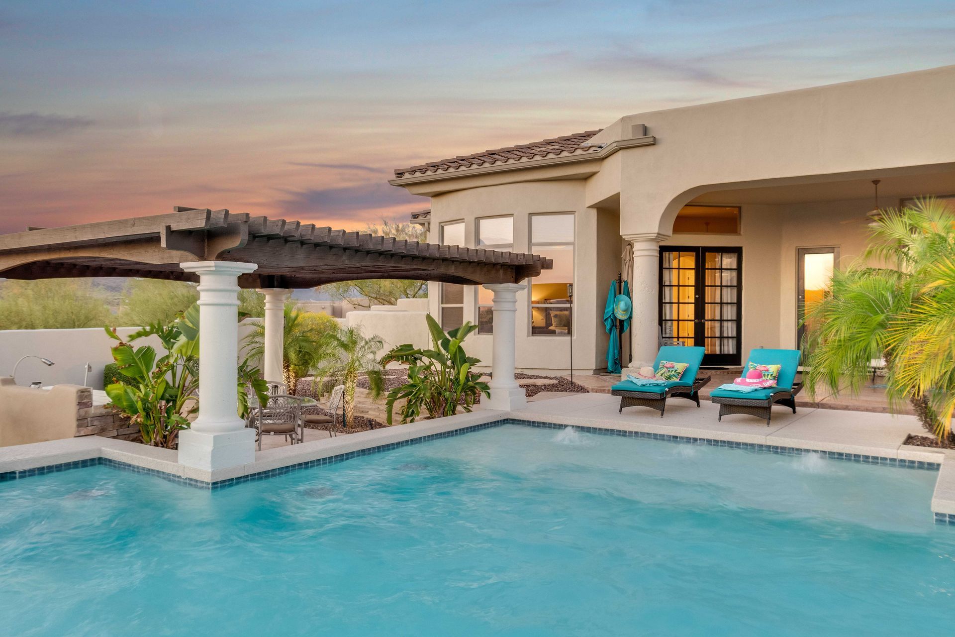 Desert villa patio with turquoise pool, pergola, and lounge chairs at sunset