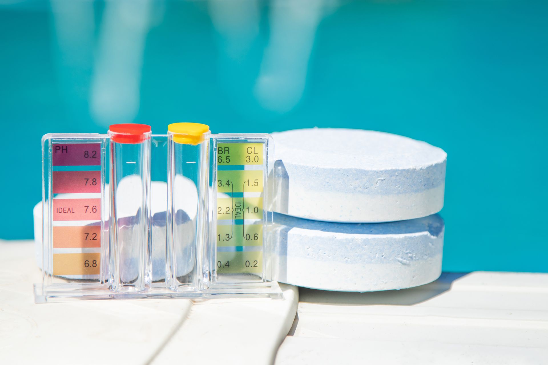 A swimming pool test kit with color-coded pH and chlorine charts and two white chemical tablets on a white deck.