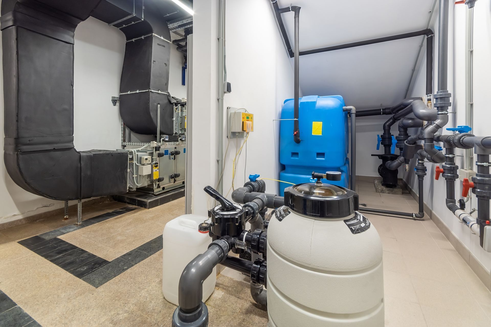 A mechanical room featuring a large blue water tank, filtration equipment, and black industrial ducting on the left.