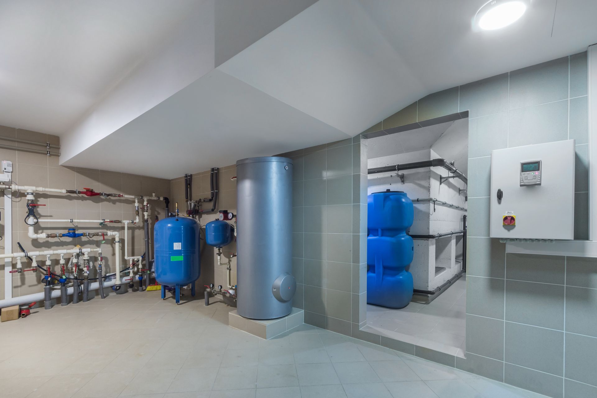 Mechanical room with white piping, a blue pressure tank, a large gray water heater, and storage tanks in a side room.
