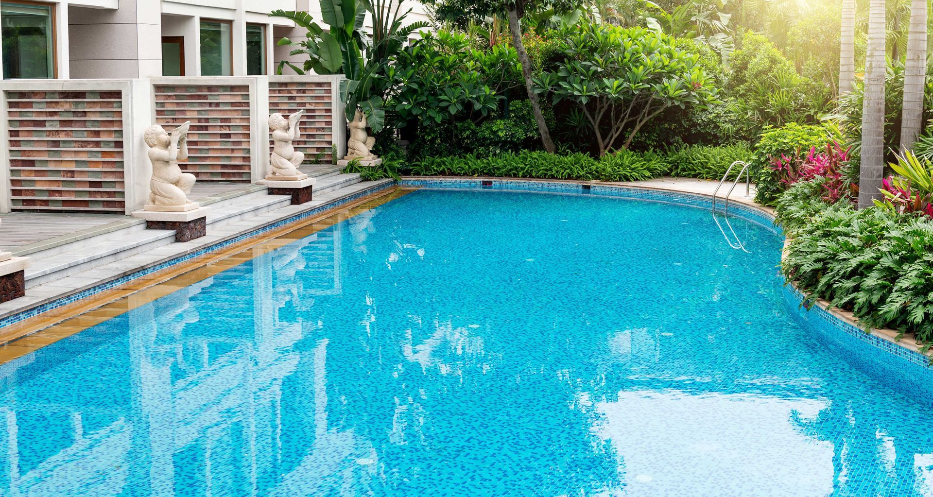 Blue backyard swimming pool beside a patio, surrounded by lush greenery and flowers