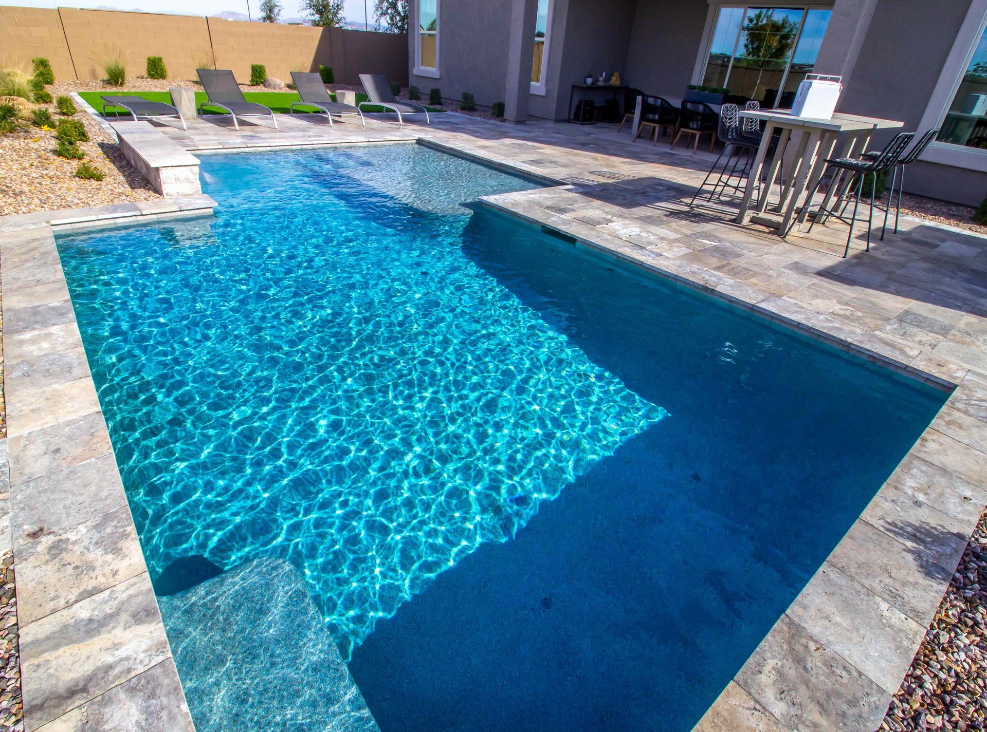 Rectangular backyard swimming pool with bright blue water and a stone patio beside it
