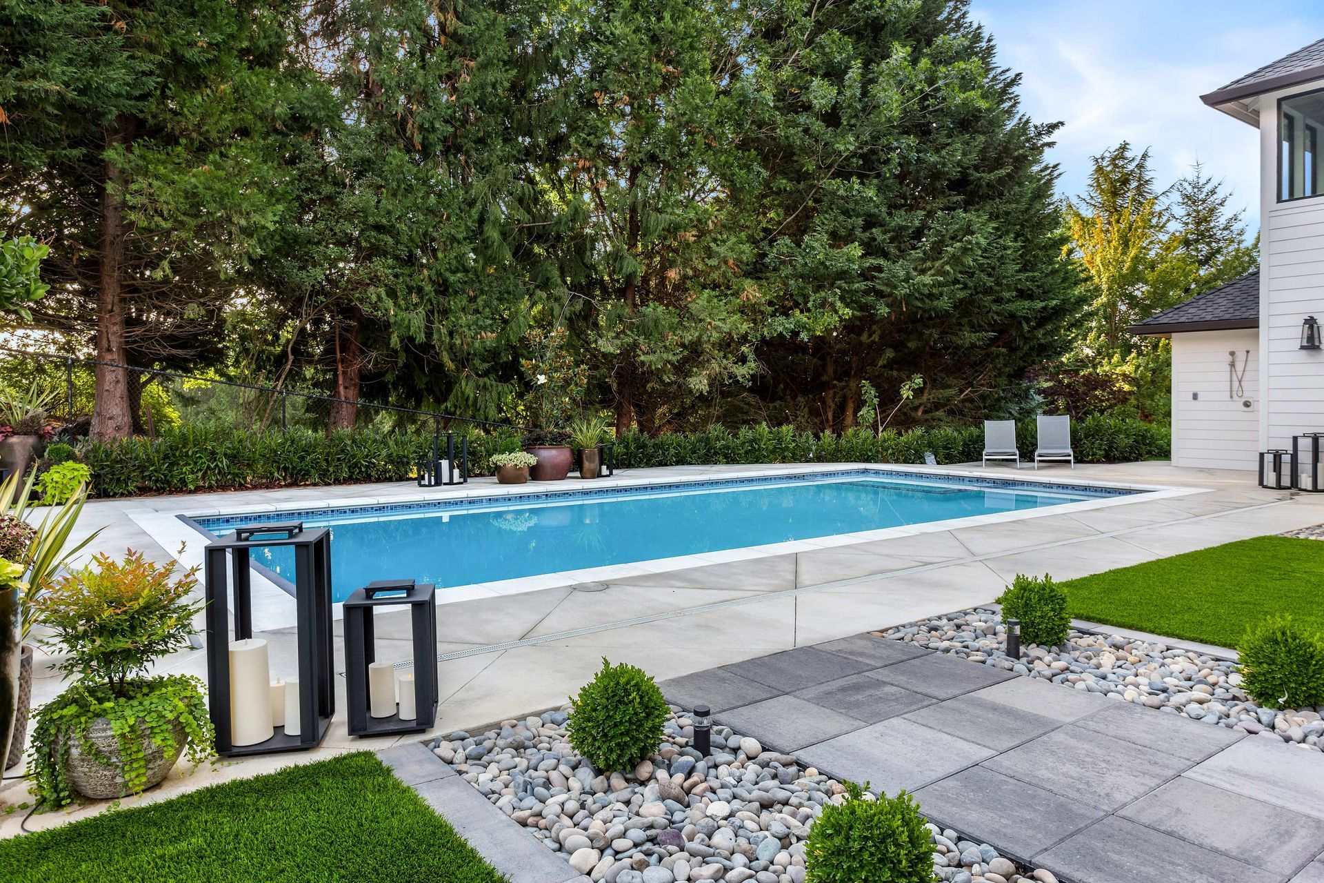 Backyard swimming pool with blue water, patio pavers, and lush green trees and shrubs