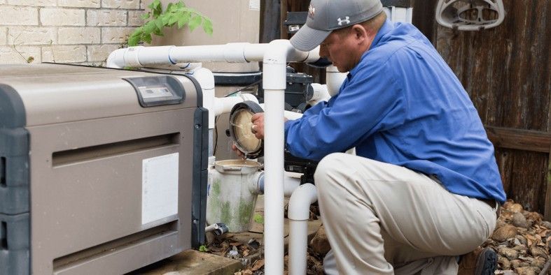 A technician in a blue shirt and cap works on pool pump equipment outdoors.