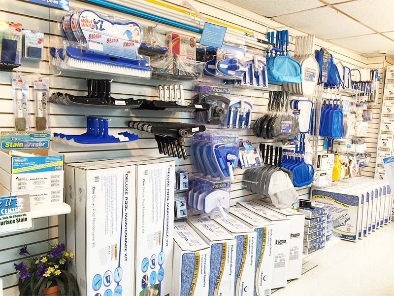 A retail store wall display stocked with blue and white pool cleaning tools, equipment, and boxed maintenance kits.