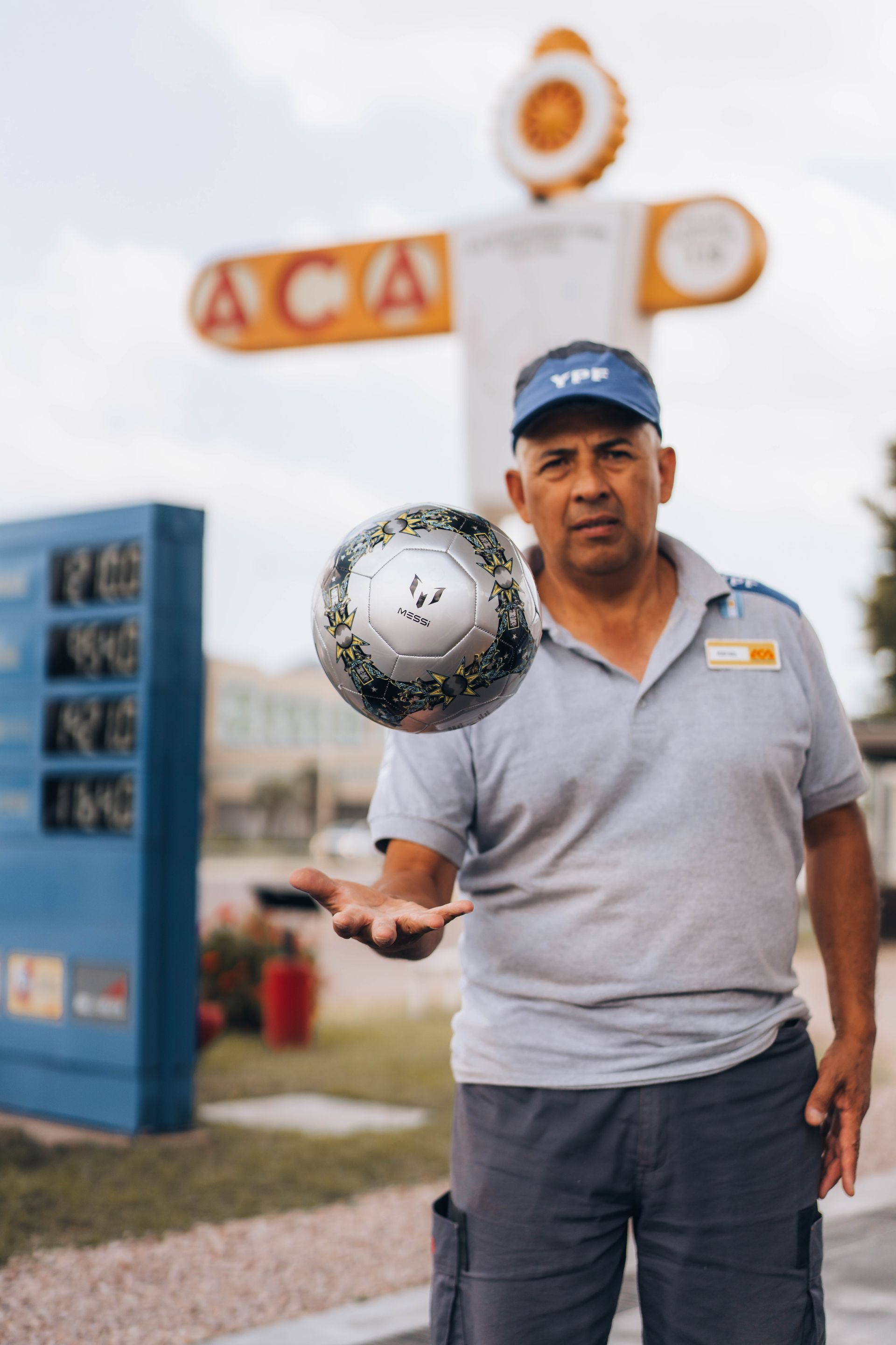 Man in uniform, holding a soccer ball, in front of a gas station sign.