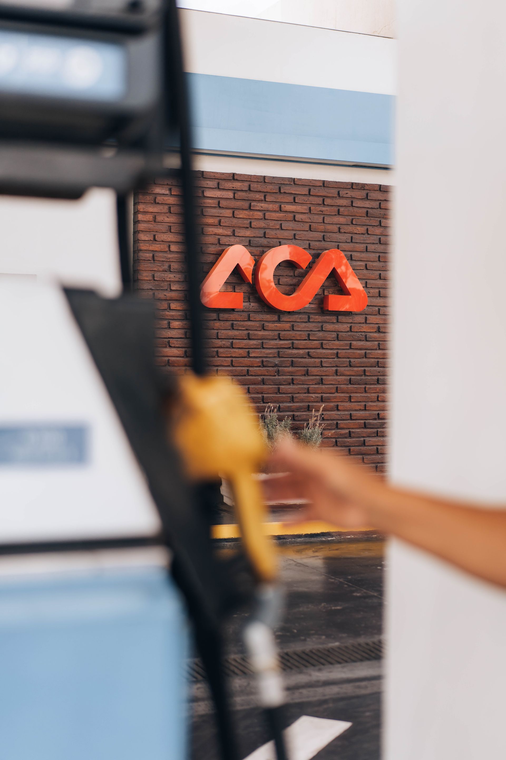 Hand reaching for gas pump nozzle with ACA logo in the background.