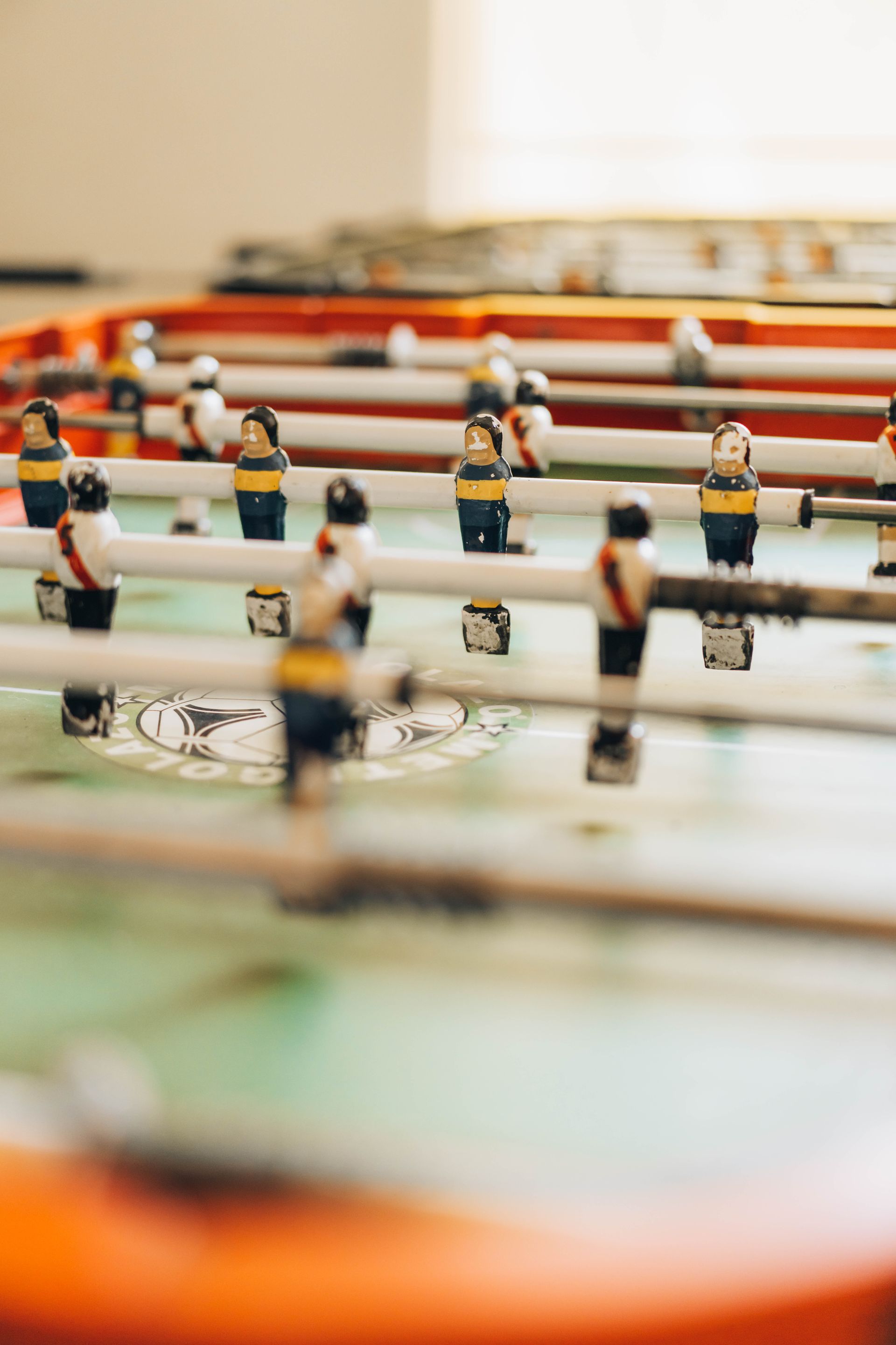 Foosball table with teams of painted figures, orange border, on green playfield.
