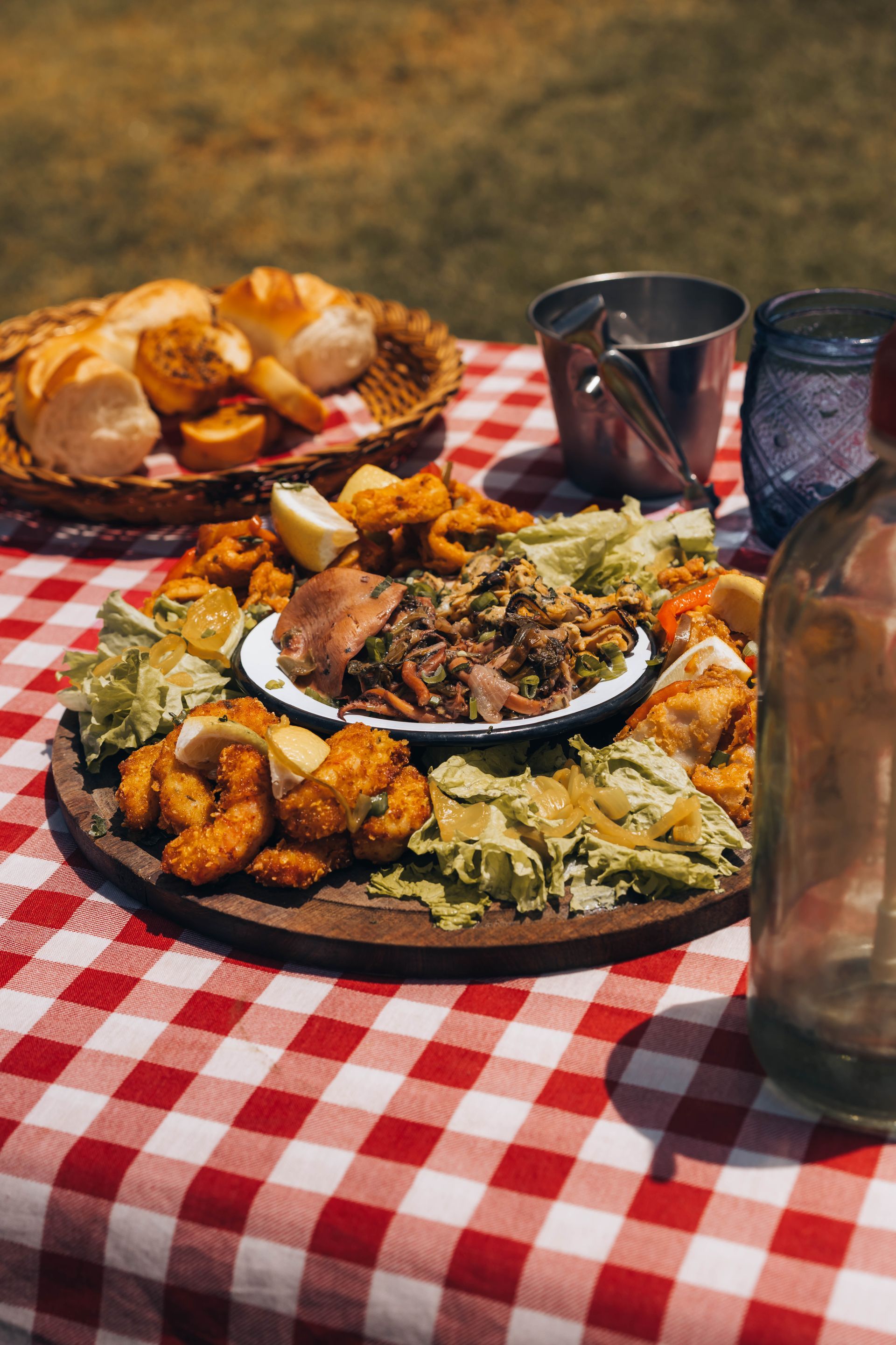 Picnic spread on red checkered tablecloth with seafood platter, bread, and drinks.