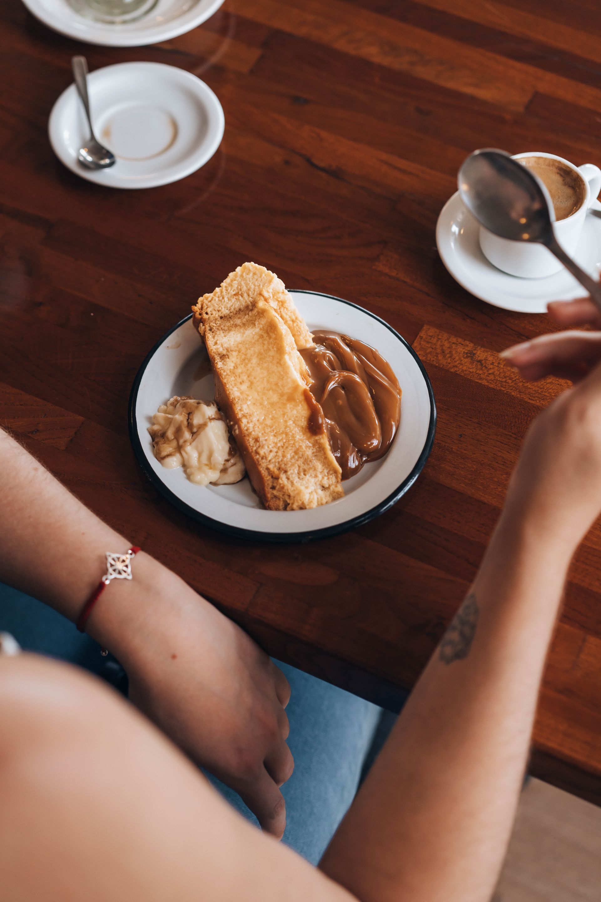 Woman's arm reaches for dessert on a plate with caramel sauce and ice cream, on a wooden table, near coffee.