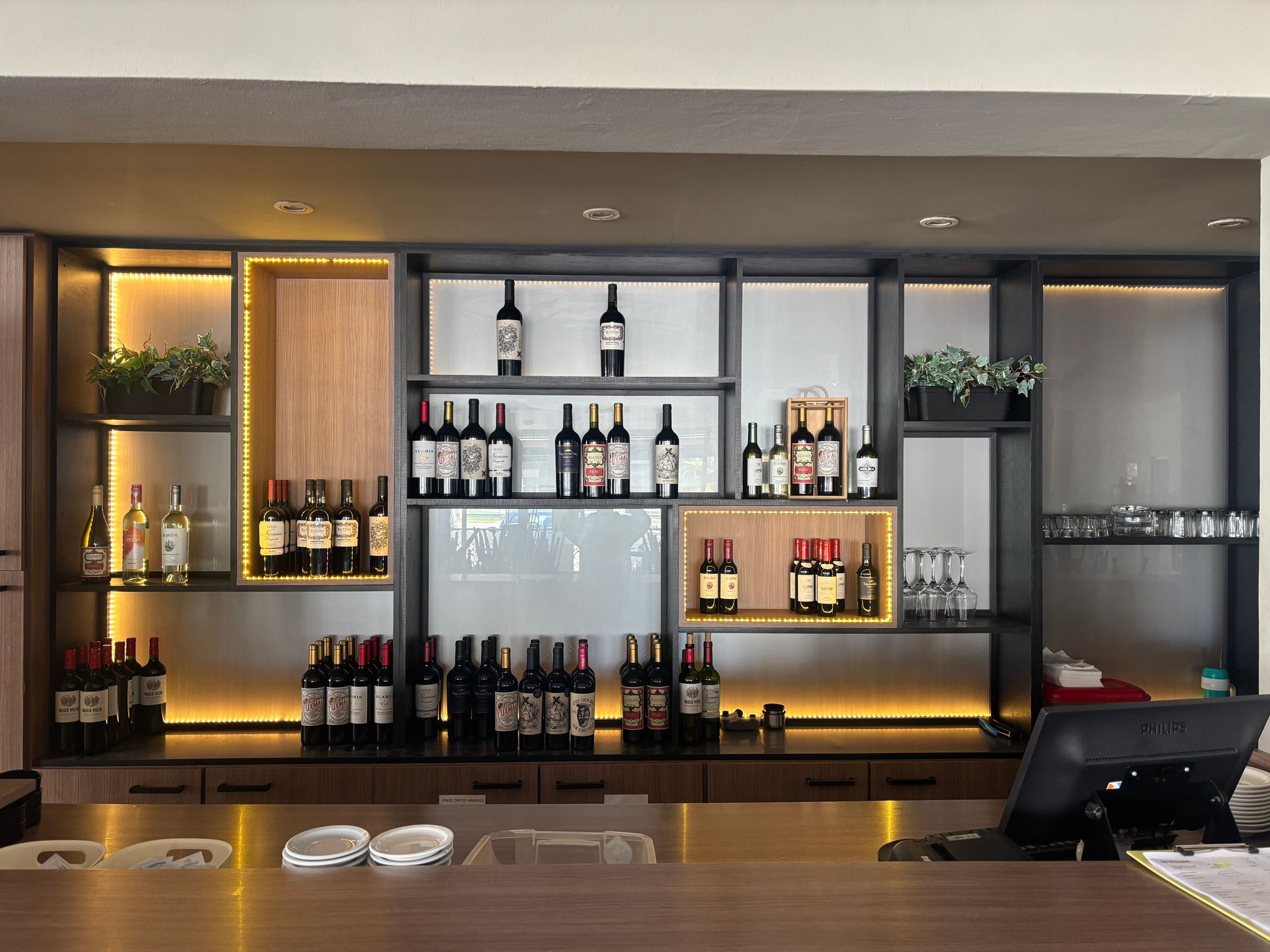 Botellas de vino expuestas en estantes con una barra al frente, iluminación cálida.
