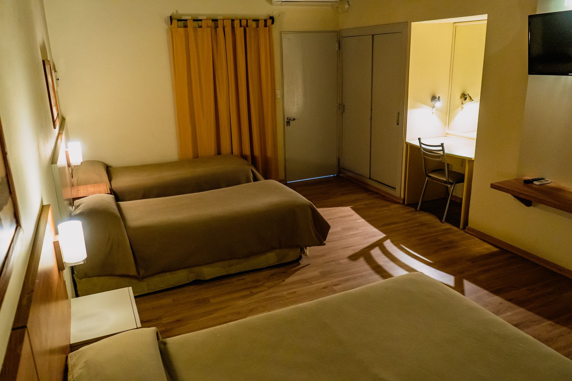 Hotel room with three beds, wood floors, and a small desk.