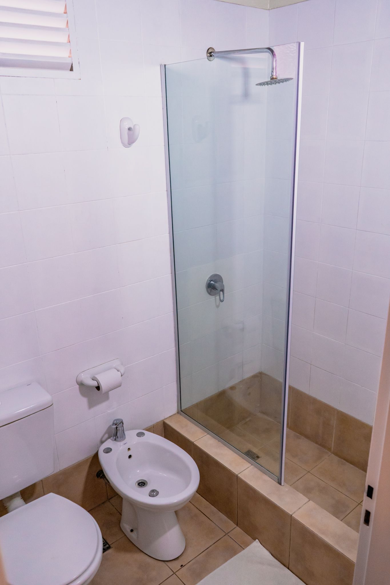 Bathroom with a toilet, bidet, and shower with glass door. White walls and tile floor.