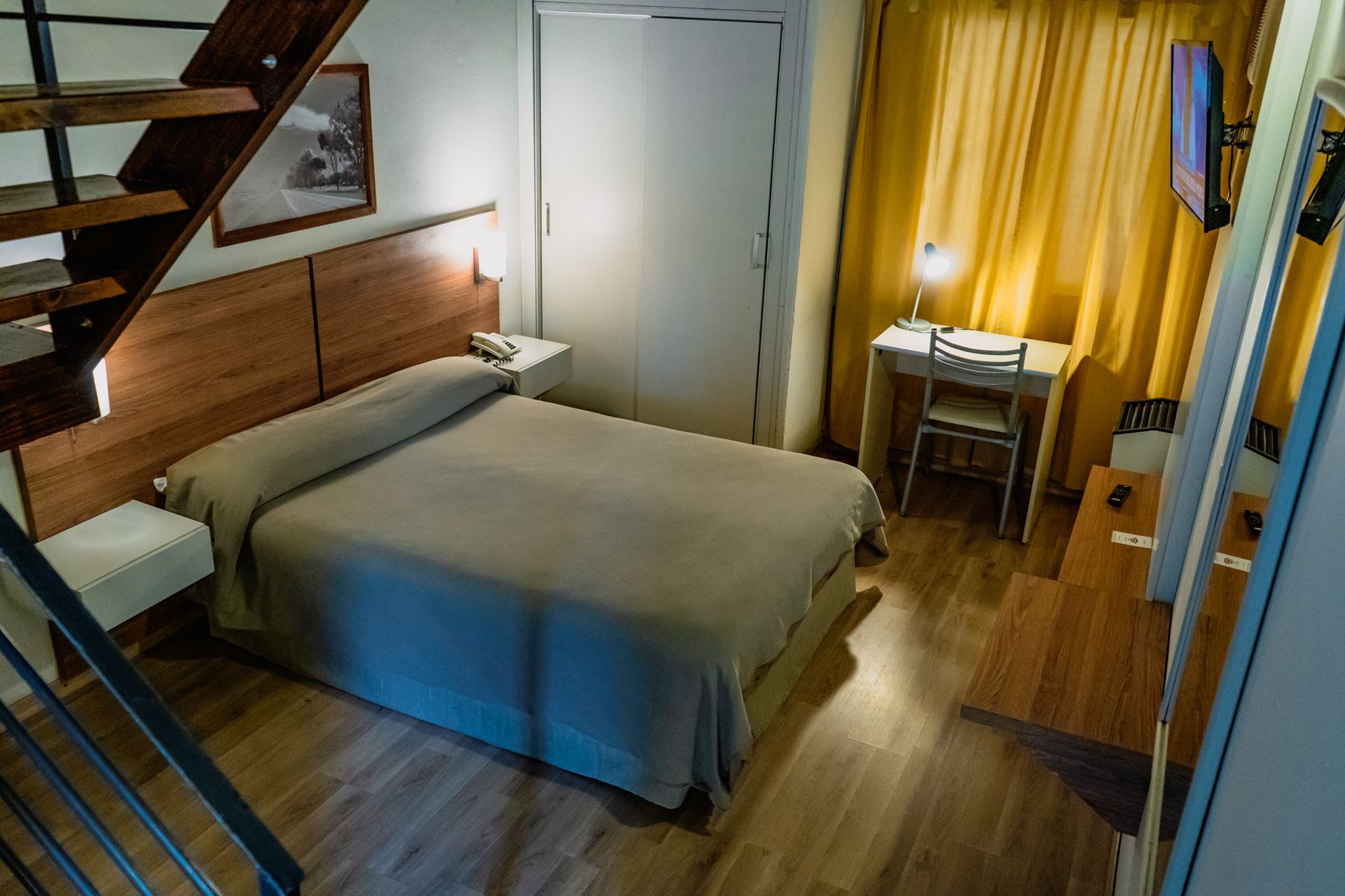 Bedroom with bed, wooden headboard, desk, stairs, yellow curtains.