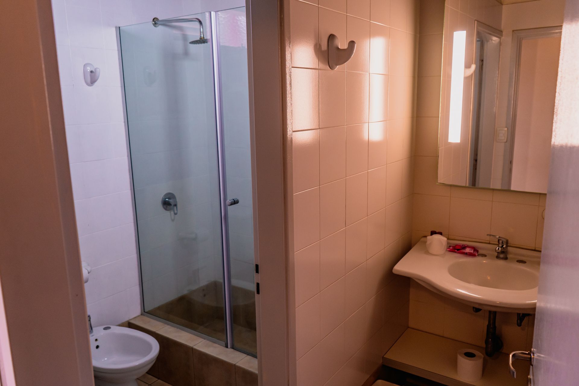 Bathroom with shower stall, toilet, sink, and mirror. Soft lighting, tile walls.