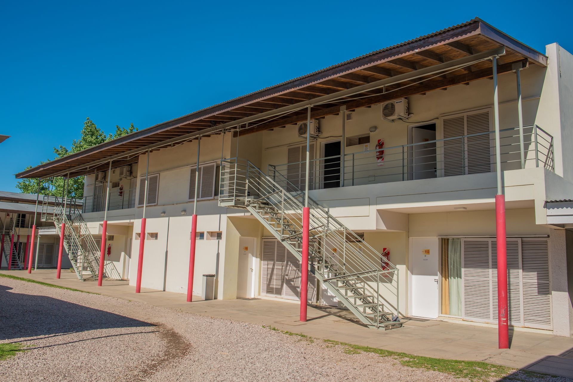 Two-story white building with red accents, exterior stairs, and a gravel path.