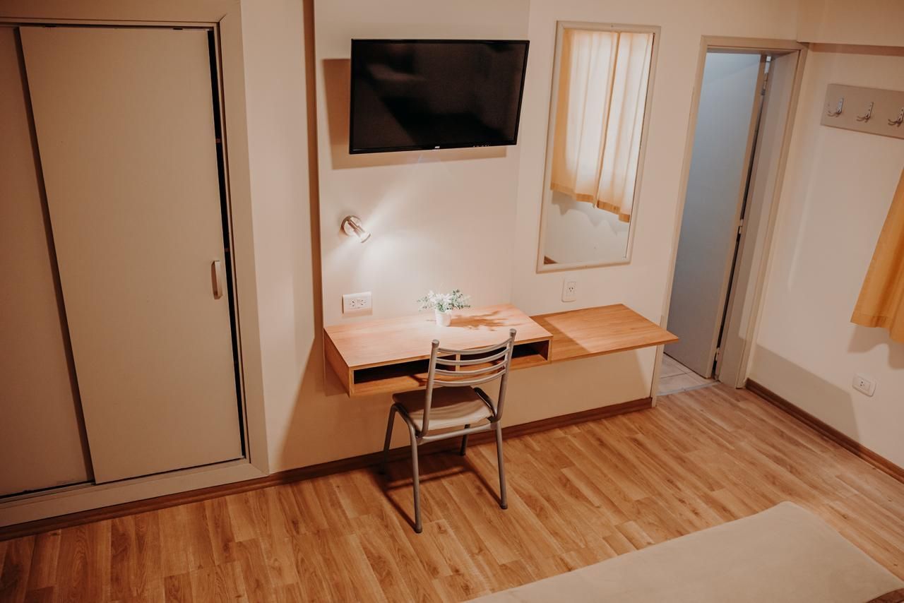 A simple room with a desk, chair, TV, closet, and a doorway.