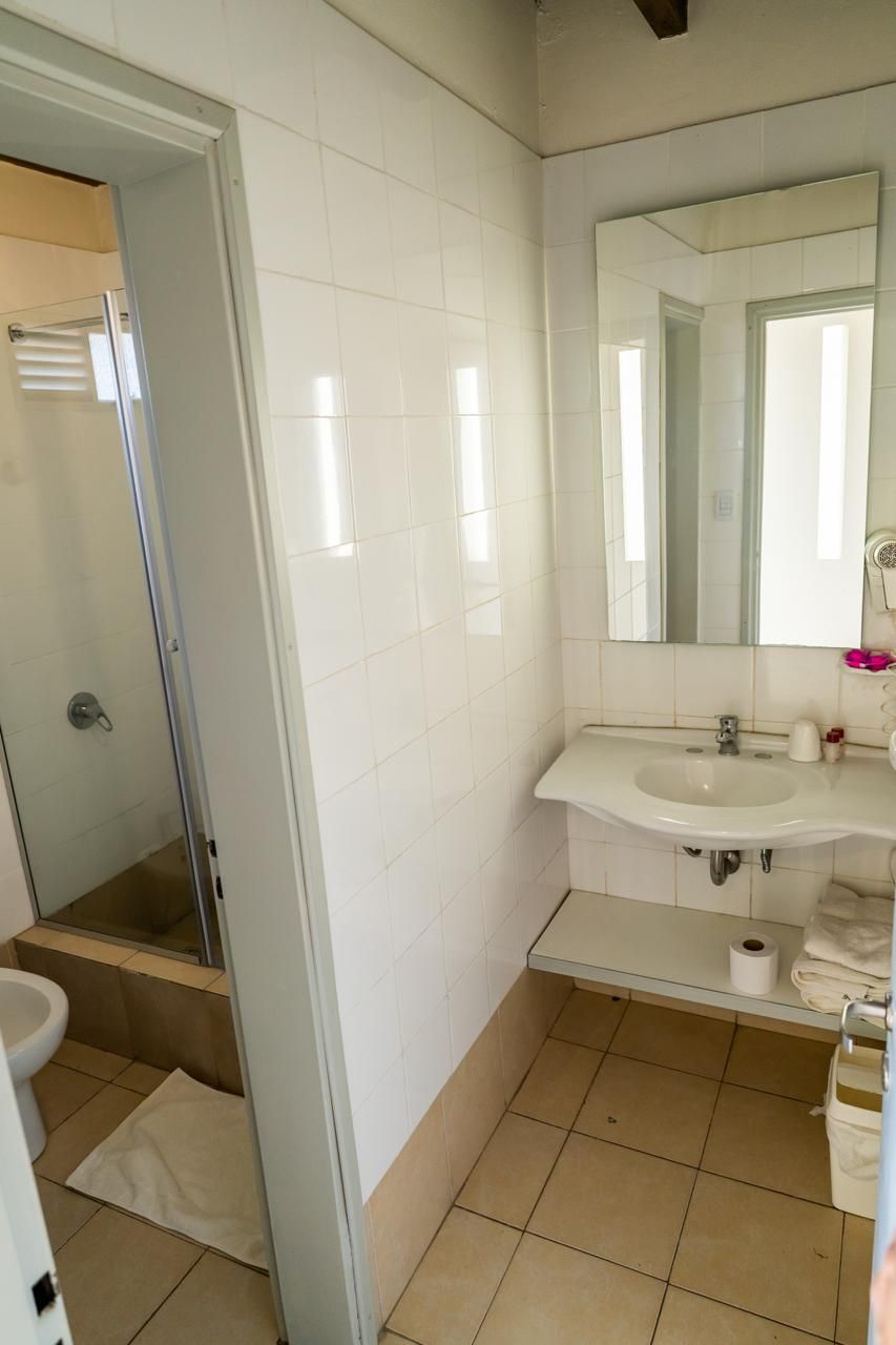 Bathroom with white tile walls, shower, sink, mirror, and toilet.