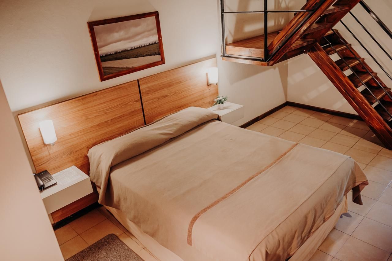 Bedroom with queen-sized bed, light-colored walls, wooden headboard, and a loft with stairs.