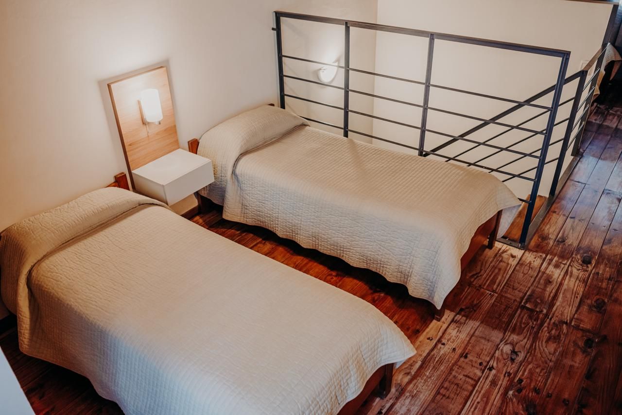Two twin beds with beige covers in a room with wooden floors and a metal railing.