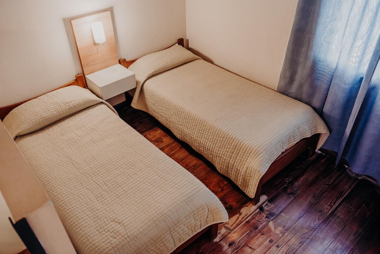 Two twin beds with beige quilts in a room with wooden floors and a nightstand.