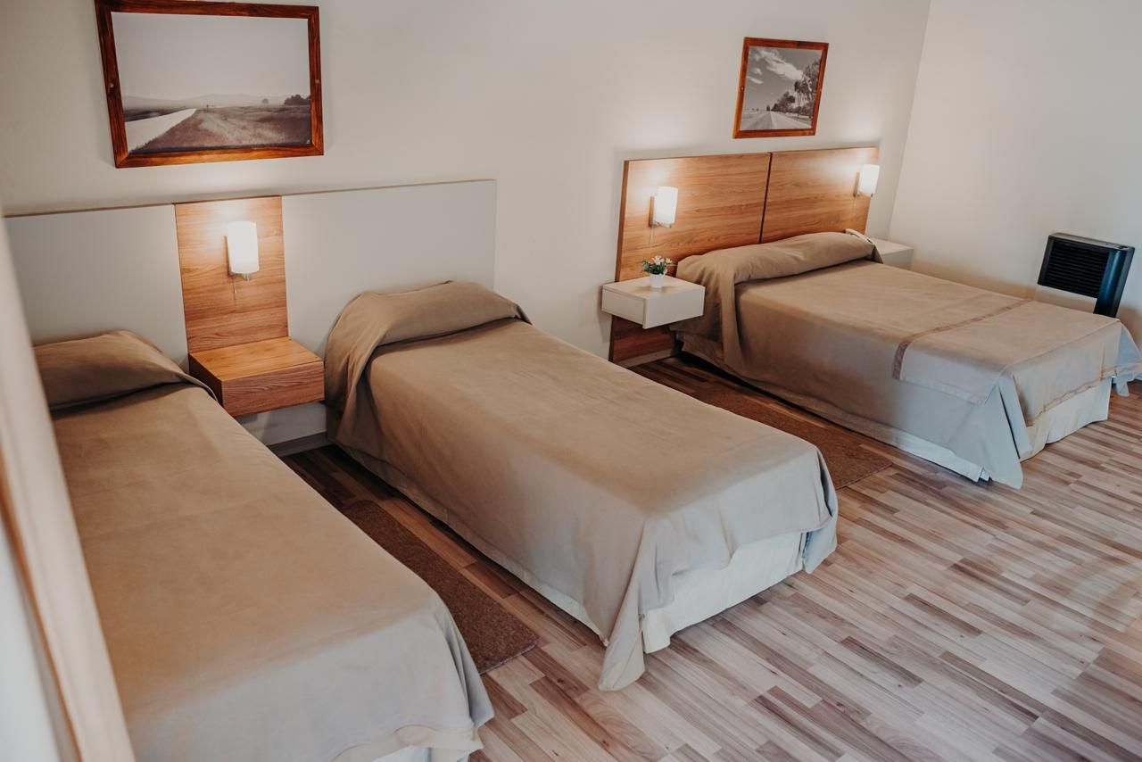 Three beds in a hotel room with brown bedding, light wood floors, and wall art.