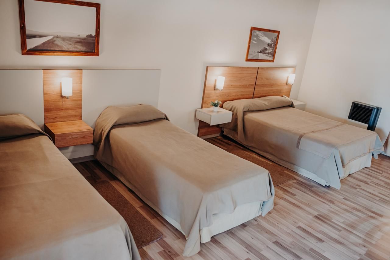 A hotel room with three single beds, neutral colors, wooden headboards, and framed art.