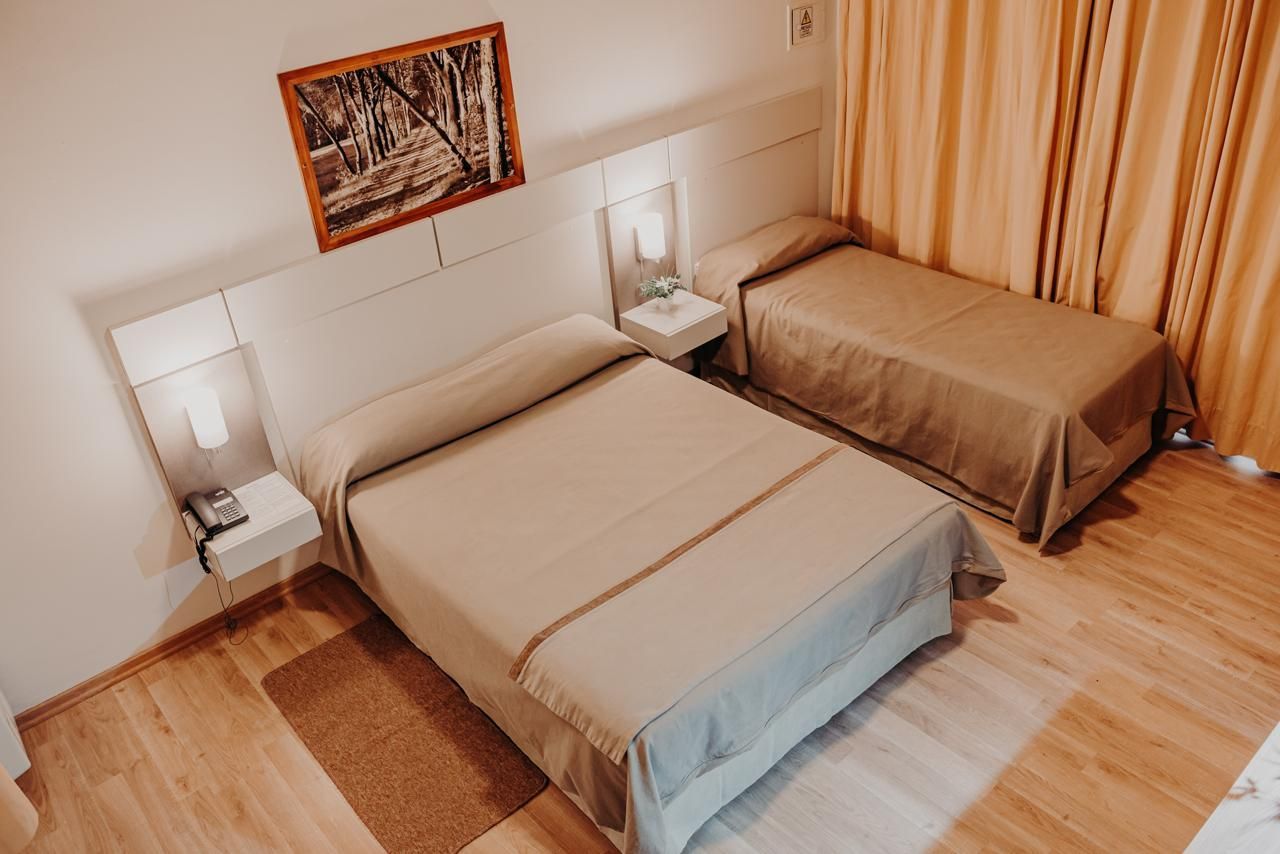 Hotel room with two beds, wood floors, beige linens, and a framed picture.