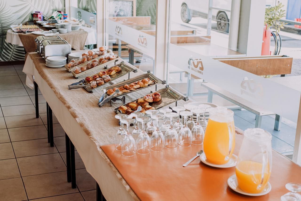 Buffet table with pastries, glasses, and juice pitchers, set up by a window.