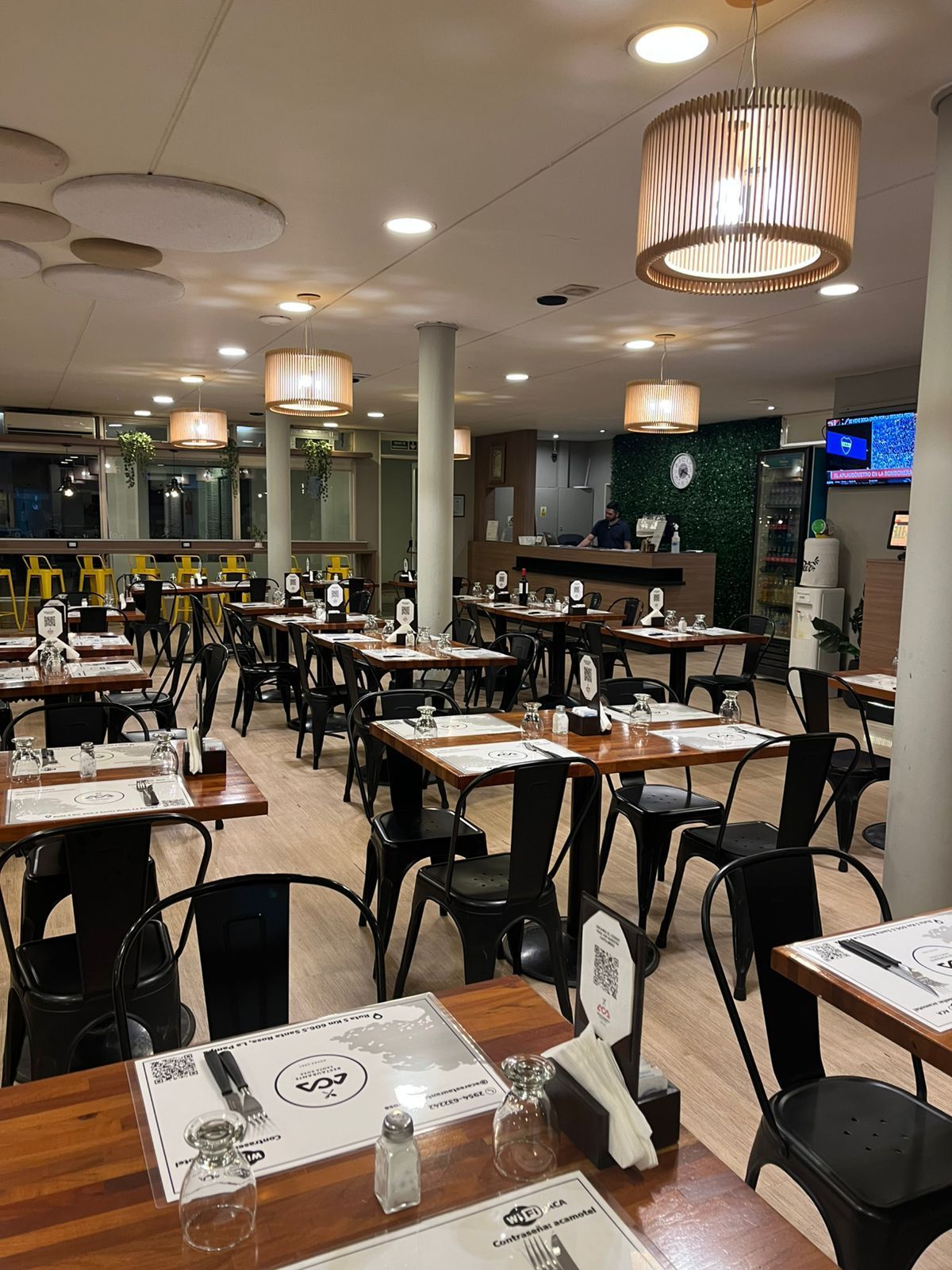 Restaurant interior with tables, chairs, and pendant lights. Black chairs, wooden tables, and neutral color scheme.