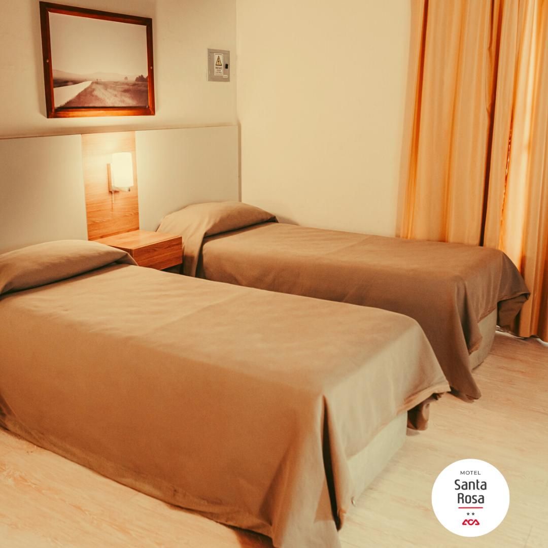 Two twin beds with beige bedding in a hotel room; painting on the wall.