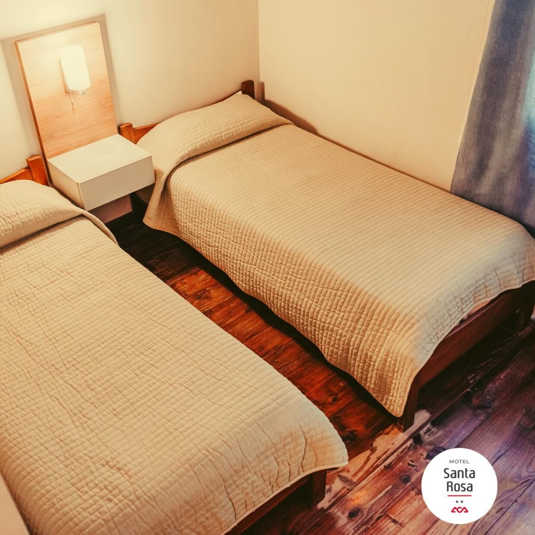 Two single beds in a bedroom; tan quilted bedspreads, wooden floor, white bedside table.