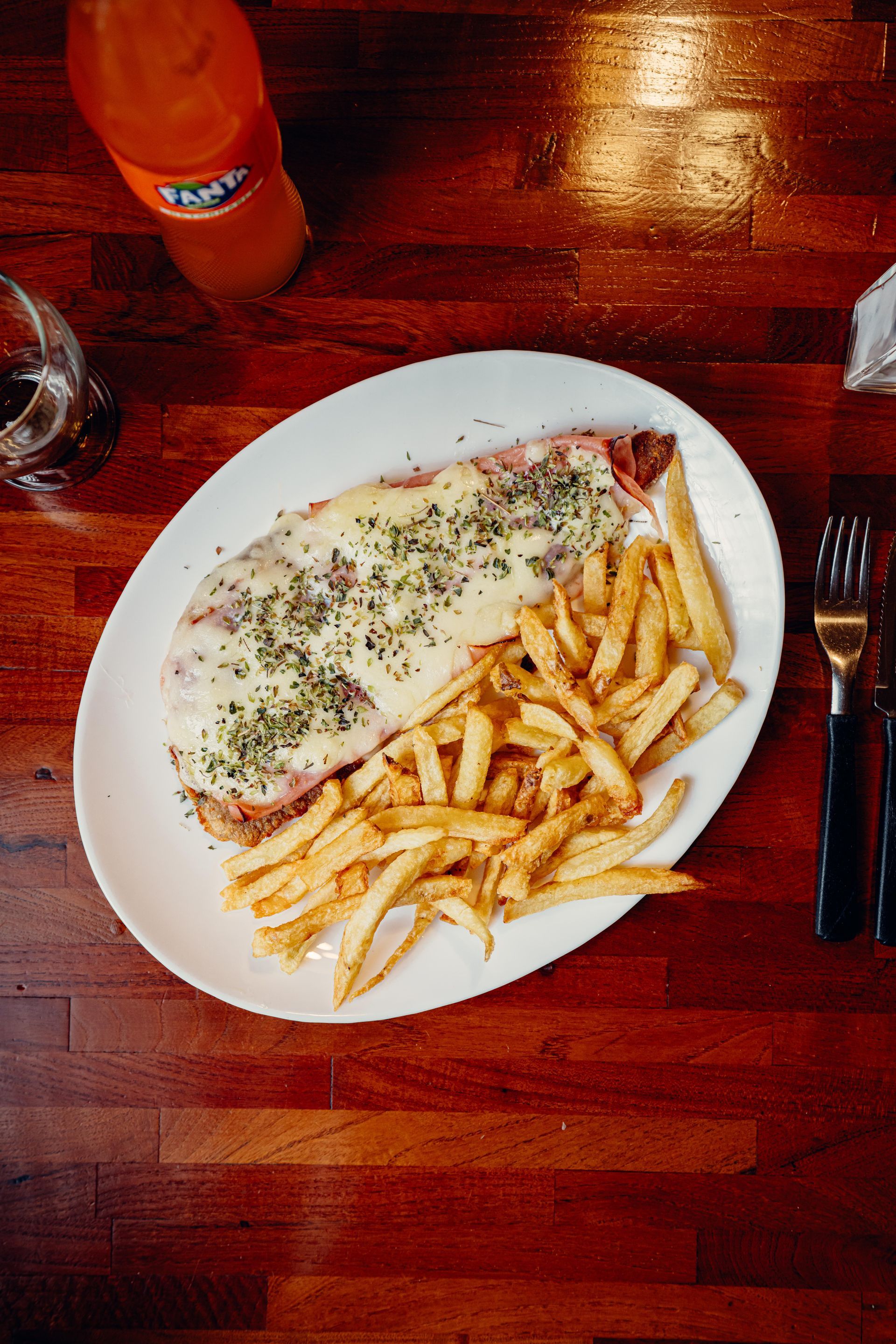 Schnitzel con patatas fritas y una botella de refresco de naranja sobre una mesa de madera.