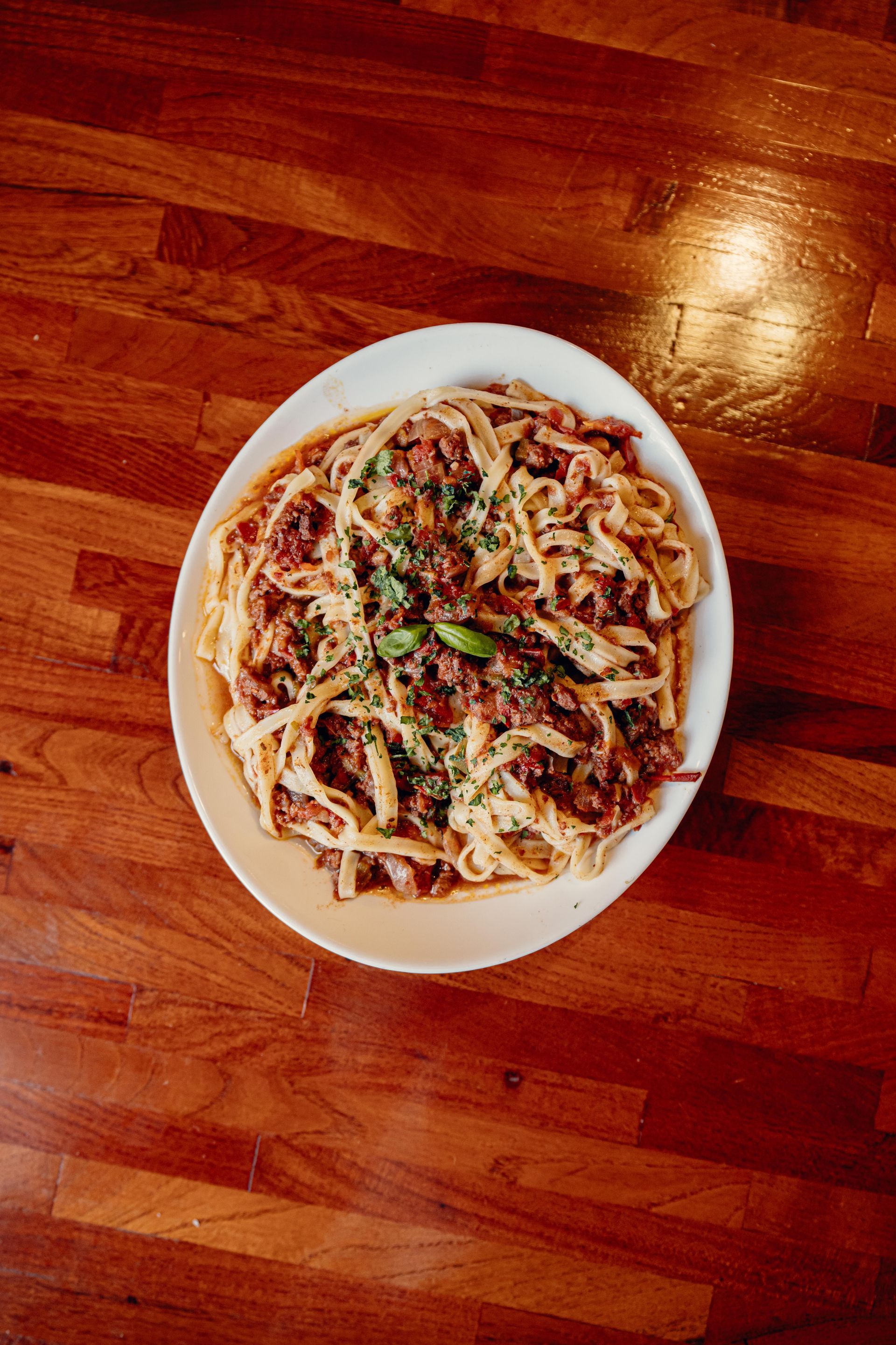 Plato de pasta con salsa de carne, adornado con hierbas, sobre una mesa de madera.