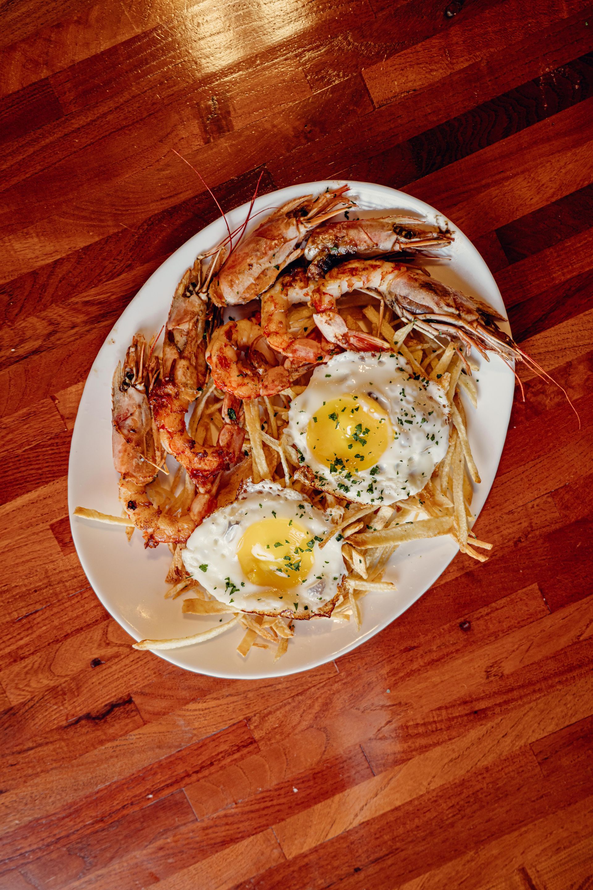 Plato de camarones y huevos fritos sobre una cama de patatas fritas en una mesa de madera.