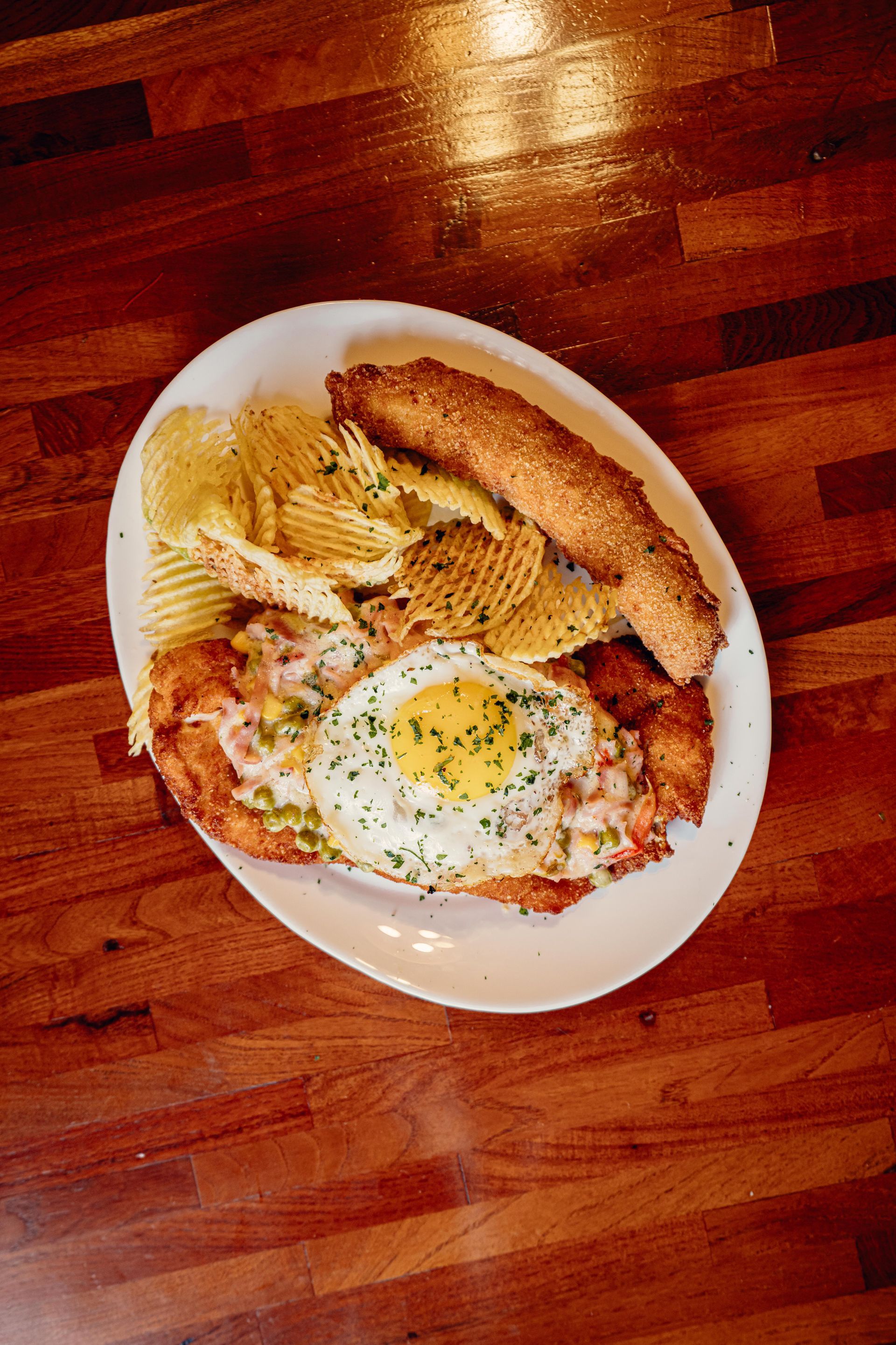 Plato con chuleta rebozada, huevo frito, patatas fritas y pan sobre una mesa de madera.