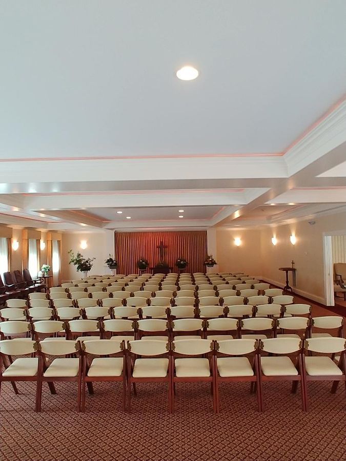 Rows of beige chairs face a small stage with a red curtain in a formal hall.