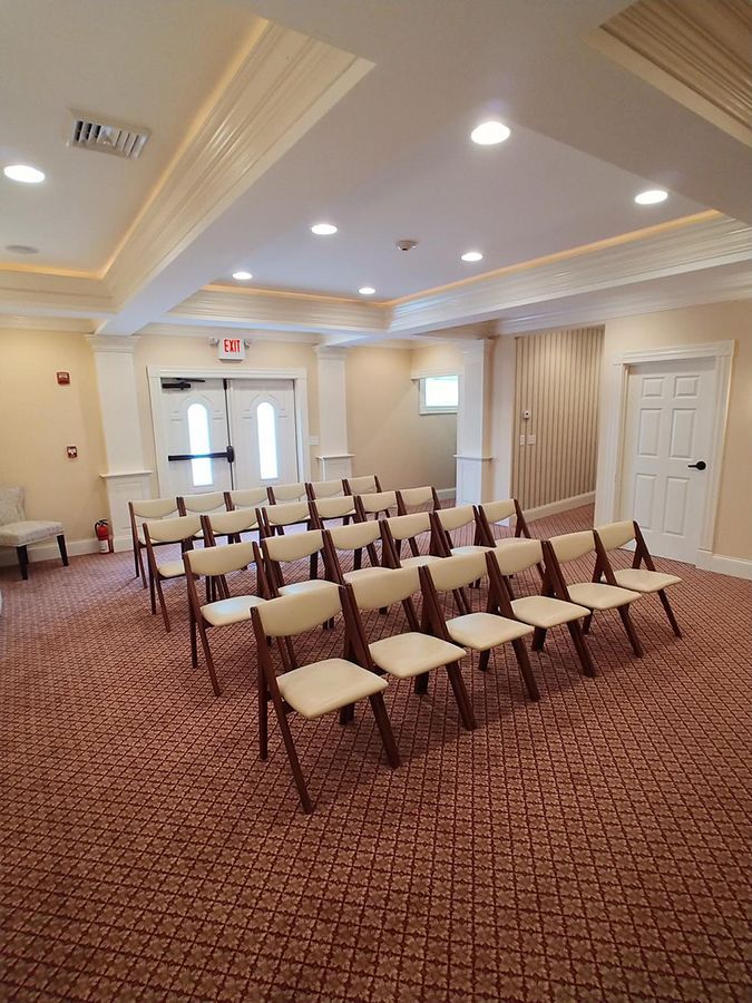 Empty room with rows of chairs, red carpet, and exit door, likely for a memorial service.