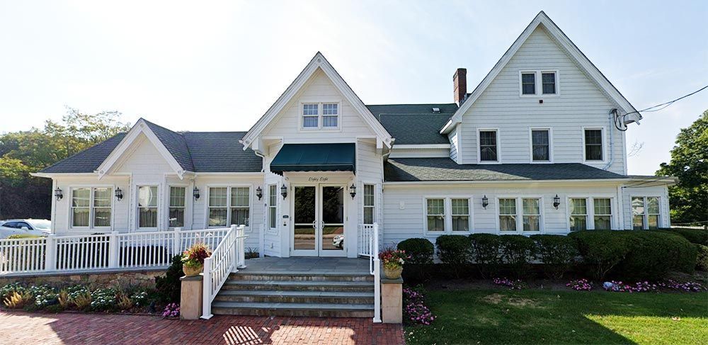 White house with steps, railing, and green awning. Landscaping and green lawn.